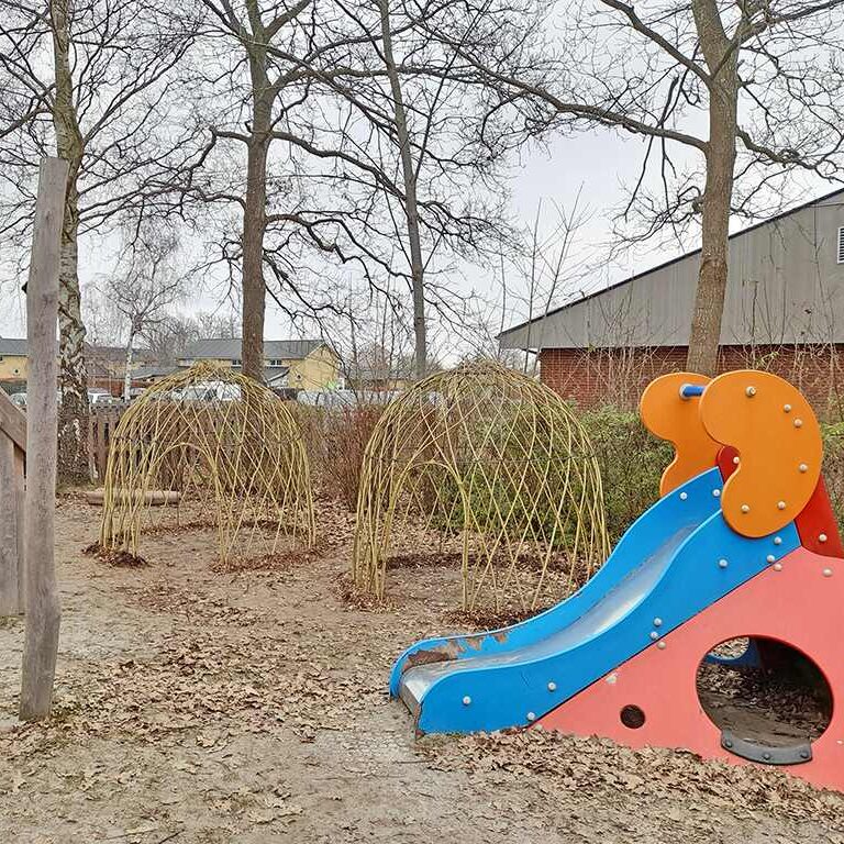 To nyflettede pilehytter på en legeplads med rutsjebane