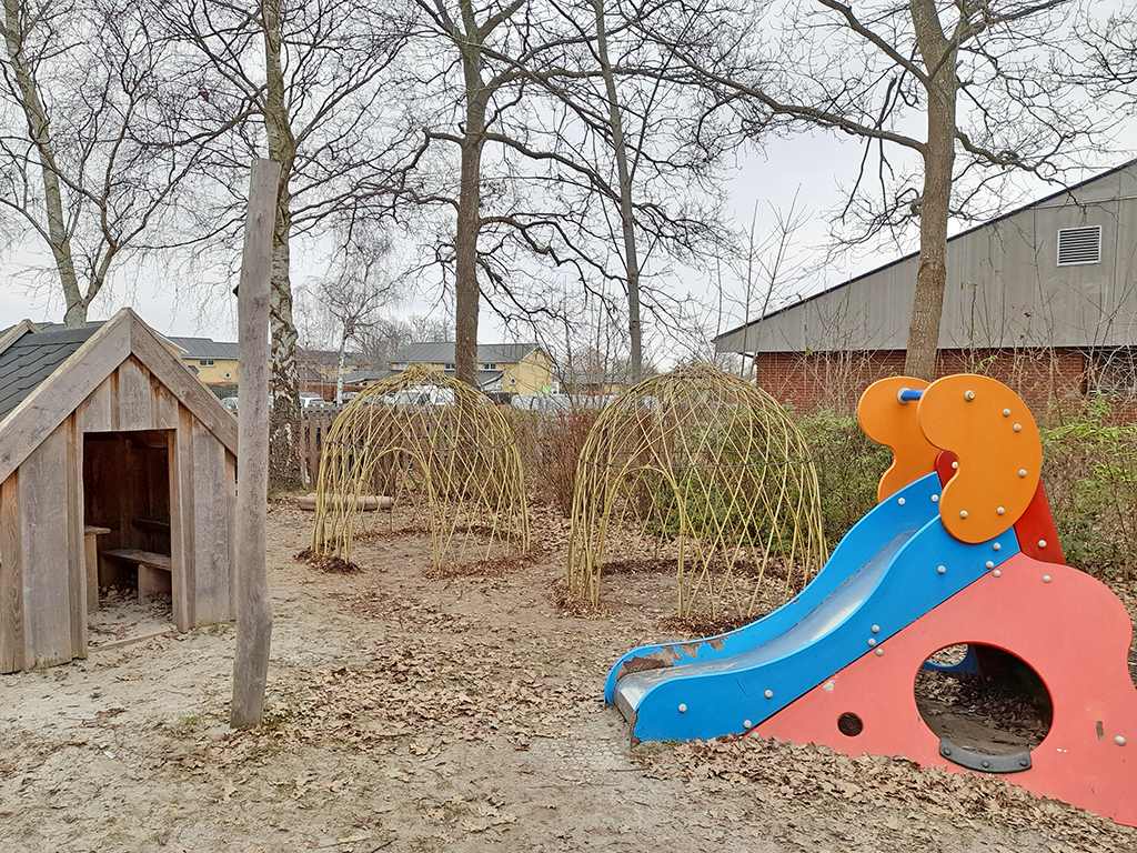 To nyflettede pilehytter på en legeplads med rutsjebane